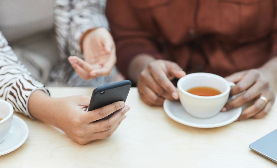 コーヒーとスマートフォンを持った2人の同僚が、共同作業の環境でアイデアを共有しています。